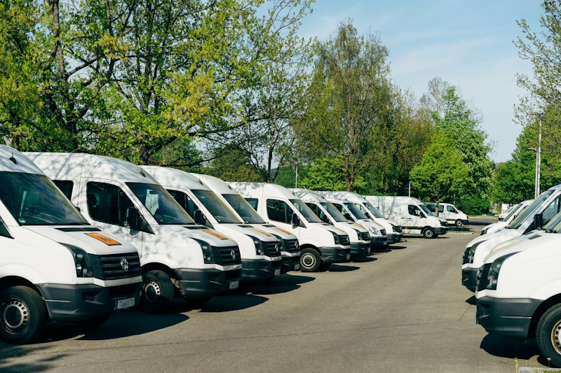 A row of white work vans parked under green trees